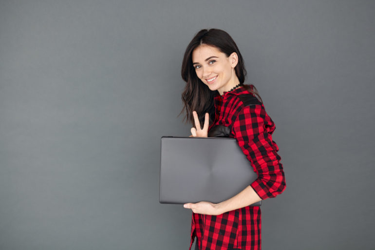young brunette woman holding laptop over grey background